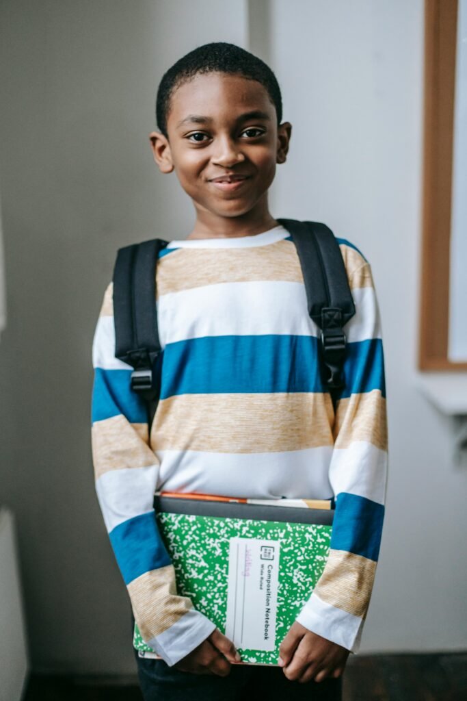 pexels-photo-5905497-5905497 Cheerful schoolboy holding books and smiling in a classroom setting, ready for learning.